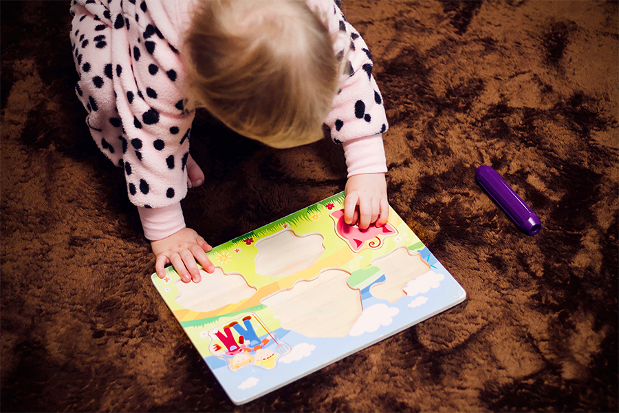blond baby in pink jumpsuit working on wood puzzle