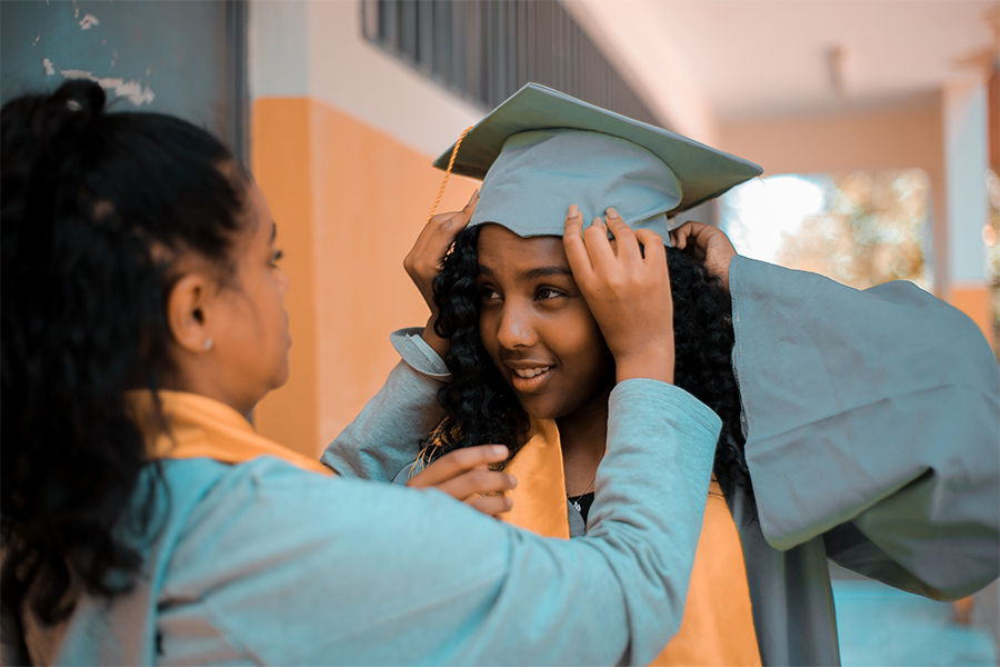 girl in blue graduation gown with another girl helping her with mortarboard