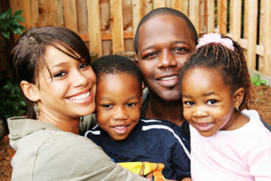 Black family smiling at camera - mom, dad, and two young children