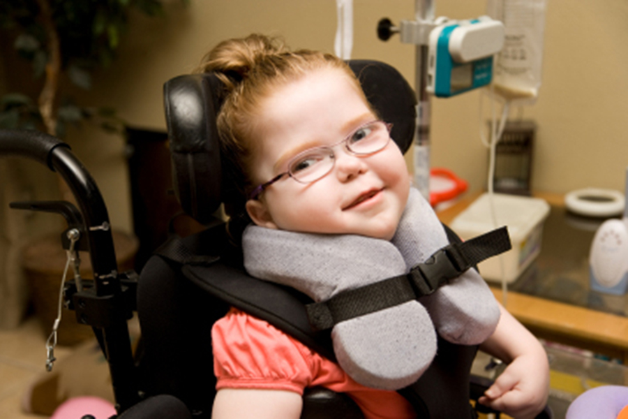child with glasses in wheelchair with head support