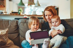 mom on couch with toddler and baby looking at tablet