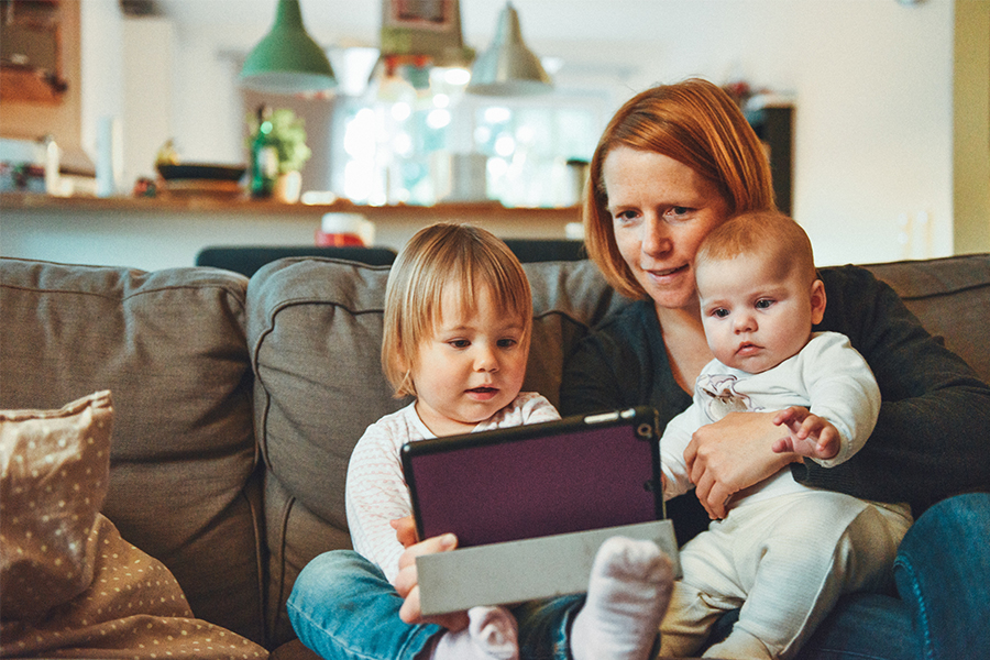 mom on couch with toddler and baby looking at tablet