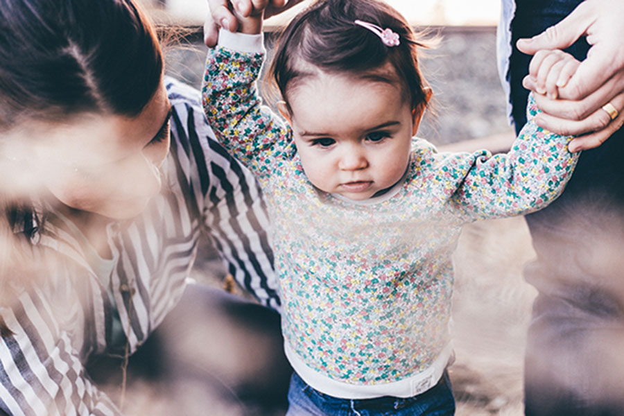 toddler holding adult's hands and walking